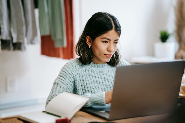 A young woman in a cozy room working on a laptop, showing concentration and dedication.